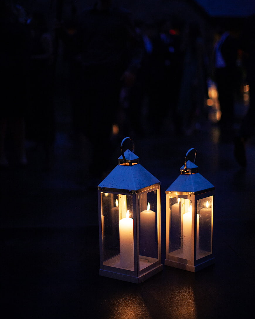 Two lit candles in metal lanterns on dark floor at night
