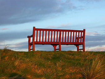 Red Wooden Bench on Grassy Hill at Sunset