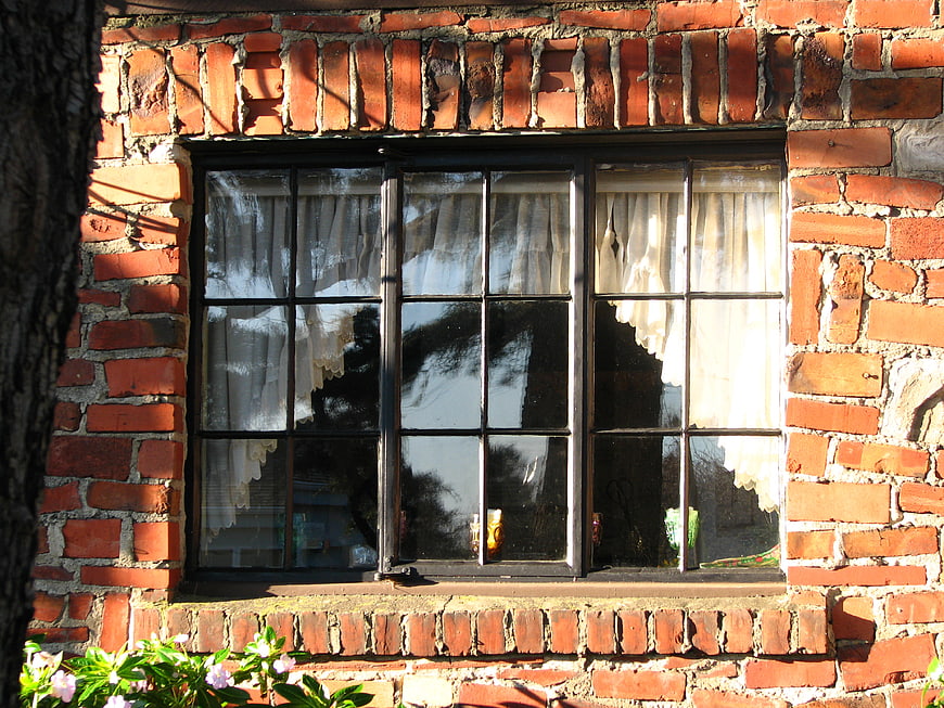 Vintage brick window with lace curtains and garden flowers