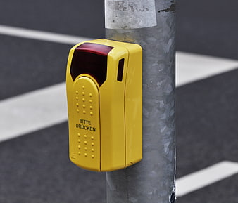 Yellow pedestrian crossing button on metal pole with blurred street background