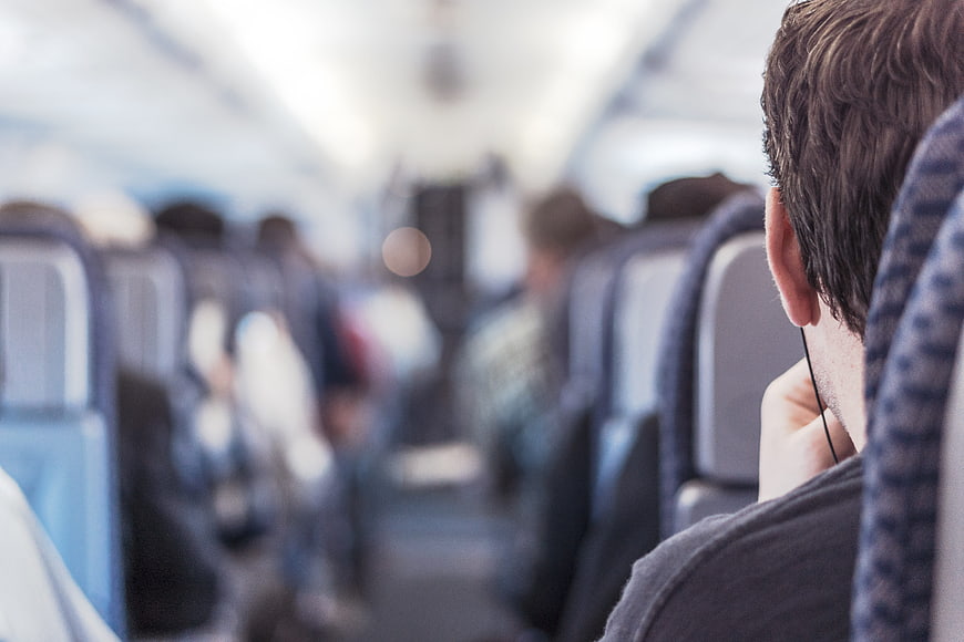 Man with earphones sitting in airplane cabin aisle