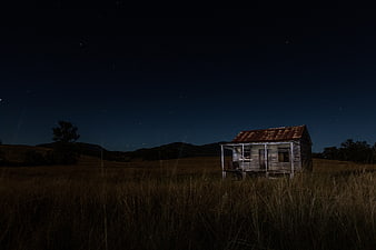 Abandoned wooden shack in grassy field under starry night sky
