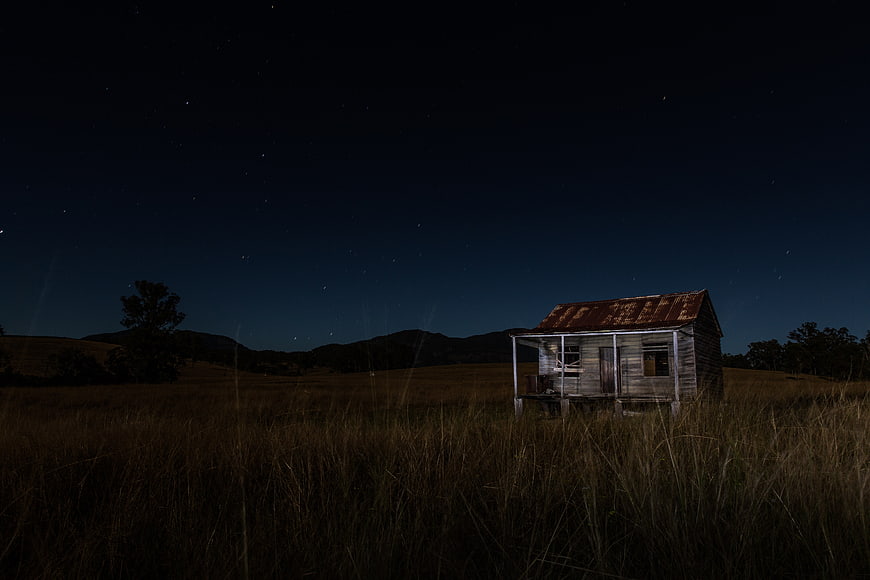 Abandoned wooden shack in grassy field under starry night sky