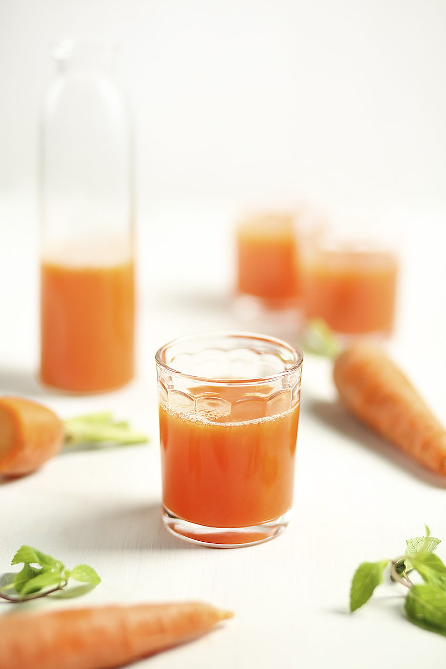 Fresh carrot juice in glass with raw carrots on white background