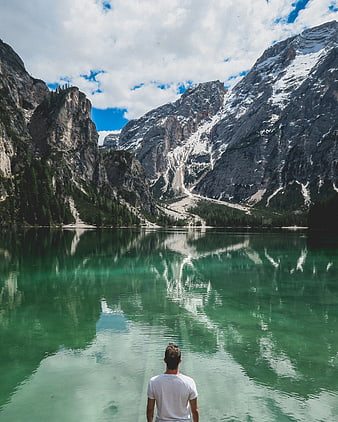 Man standing by turquoise alpine lake with mountain reflections