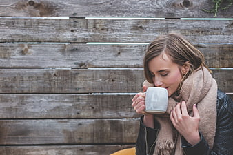 Woman drinking coffee with scarf against wooden wall