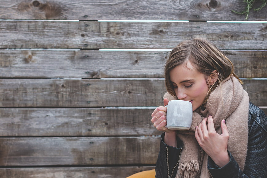 Woman drinking coffee with scarf against wooden wall