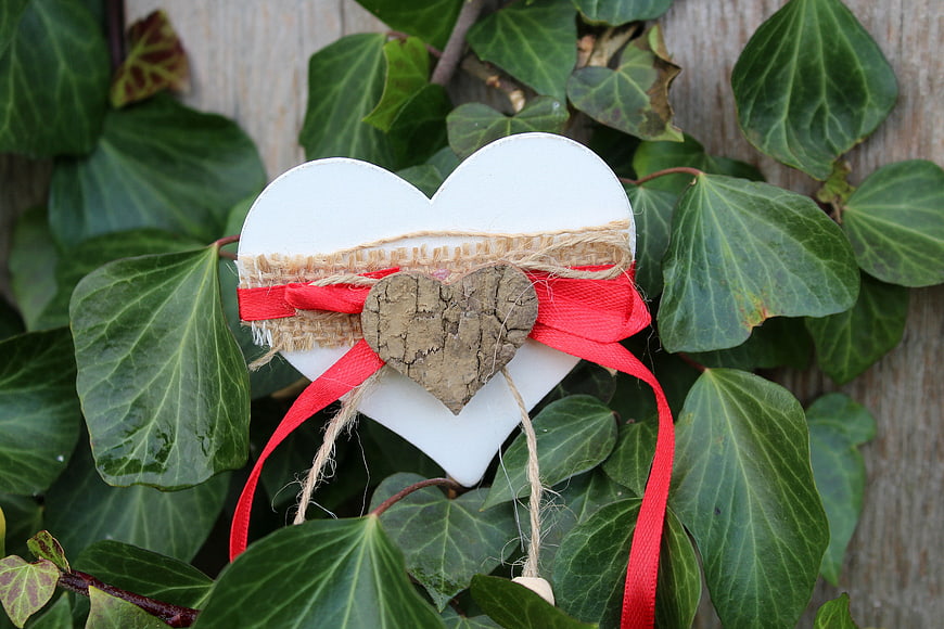 White wooden heart ornament with red ribbon on ivy leaves