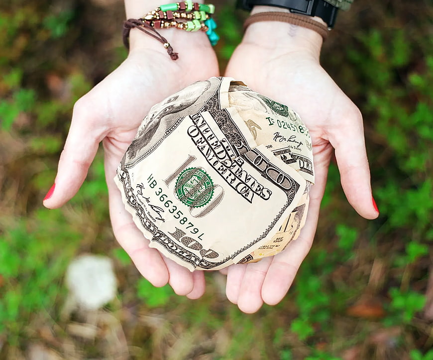 Hands holding crumpled hundred dollar bills outdoors
