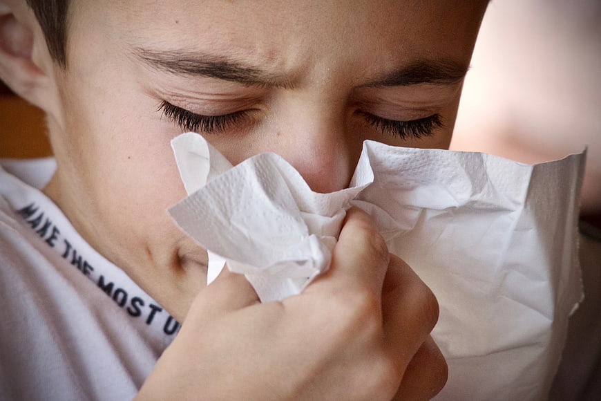 Close-up of young boy blowing nose with white tissue