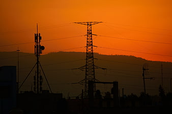 Silhouette of power lines and cell tower against orange sunset