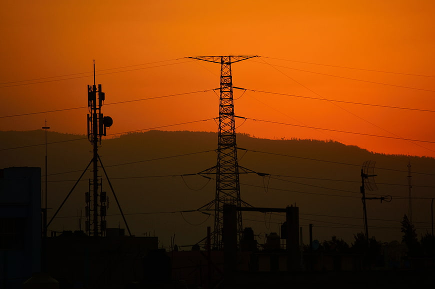 Silhouette of power lines and cell tower against orange sunset