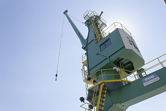 Low angle view of green industrial port crane against blue sky
