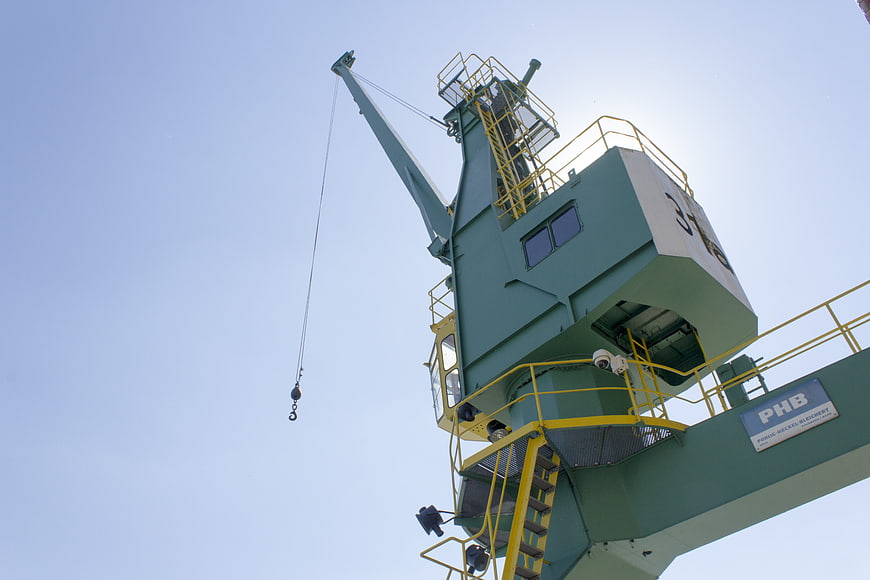 Low angle view of green industrial port crane against blue sky