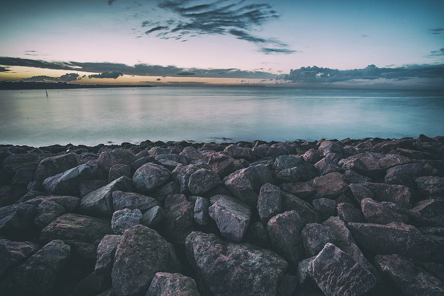 Coastal rocks and calm sea at dusk with dramatic clouds