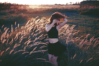 Woman in Black Outfit Standing in Tall Grass at Sunset