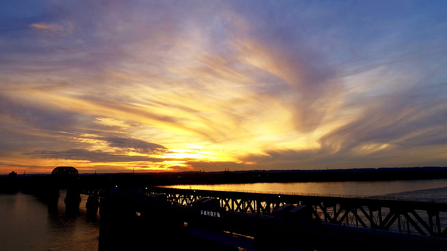 Dramatic sunset over river bridge with golden clouds