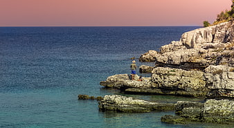 Man Fishing on Rocky Coastline at Sunset