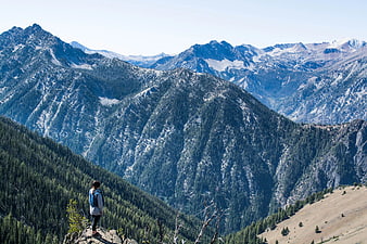 Hiker Standing on Cliff Overlooking Snowy Mountain Range