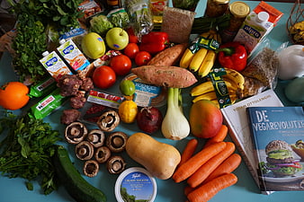Flat lay of fresh vegan groceries and cookbooks on blue table