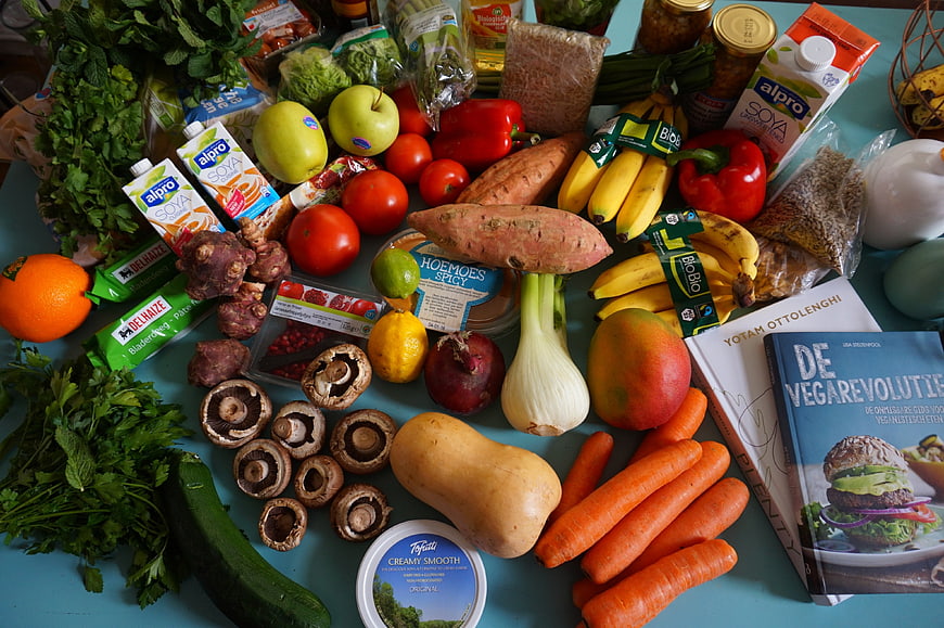 Flat lay of fresh vegan groceries and cookbooks on blue table