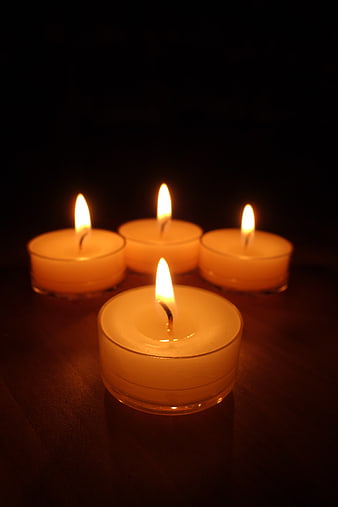 Four Lit Tea Light Candles on Dark Wooden Surface