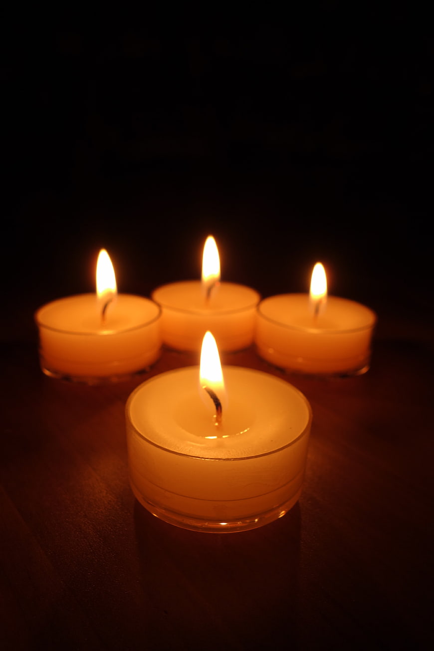 Four Lit Tea Light Candles on Dark Wooden Surface