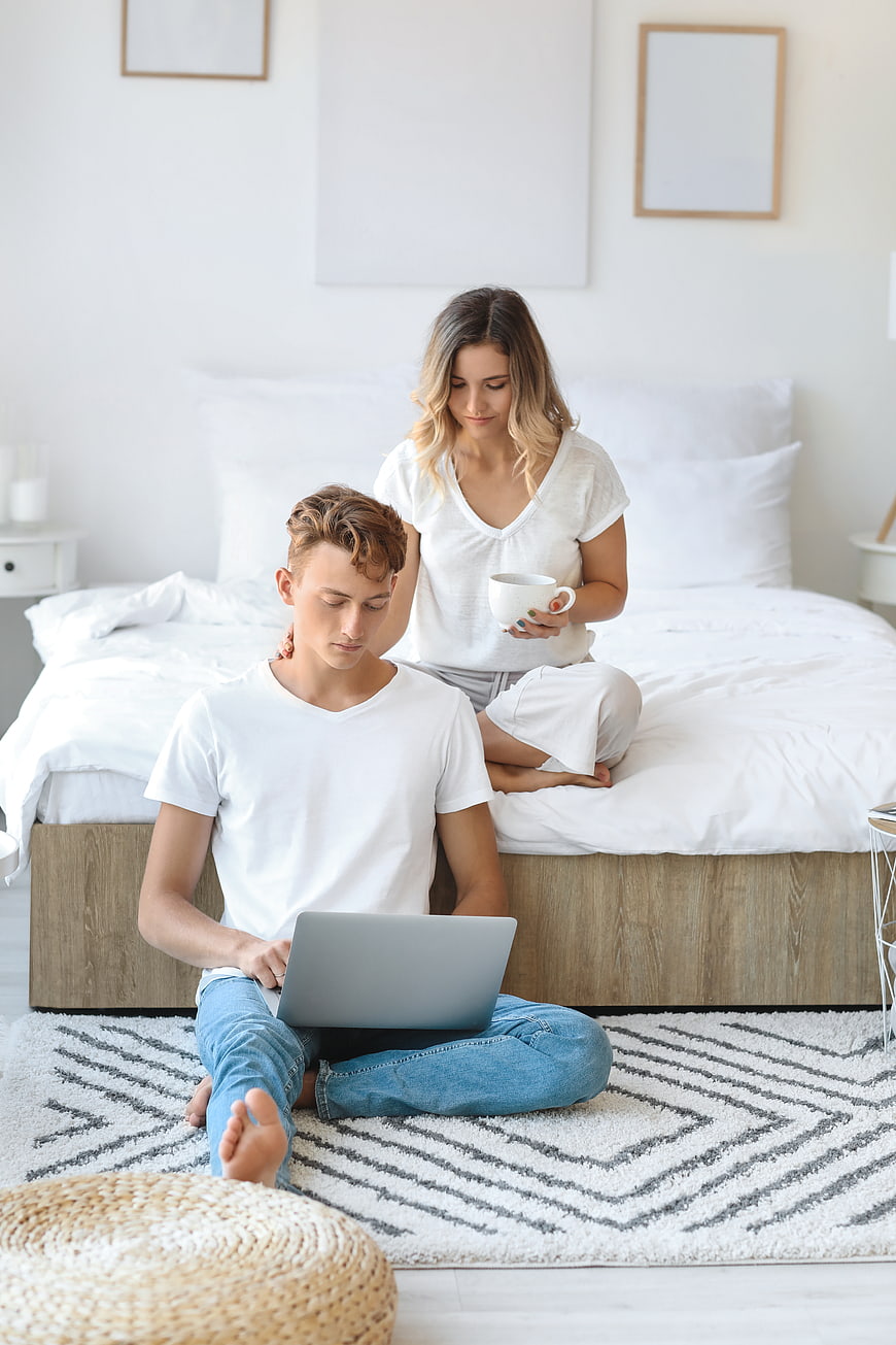 Young couple relaxing in bedroom with laptop and coffee