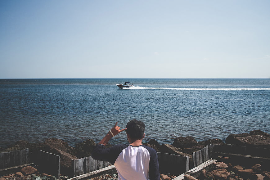 Man Gesturing at Speedboat on Ocean Horizon