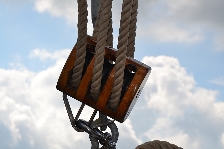 Close-up of wooden ship pulley block with rope against sky