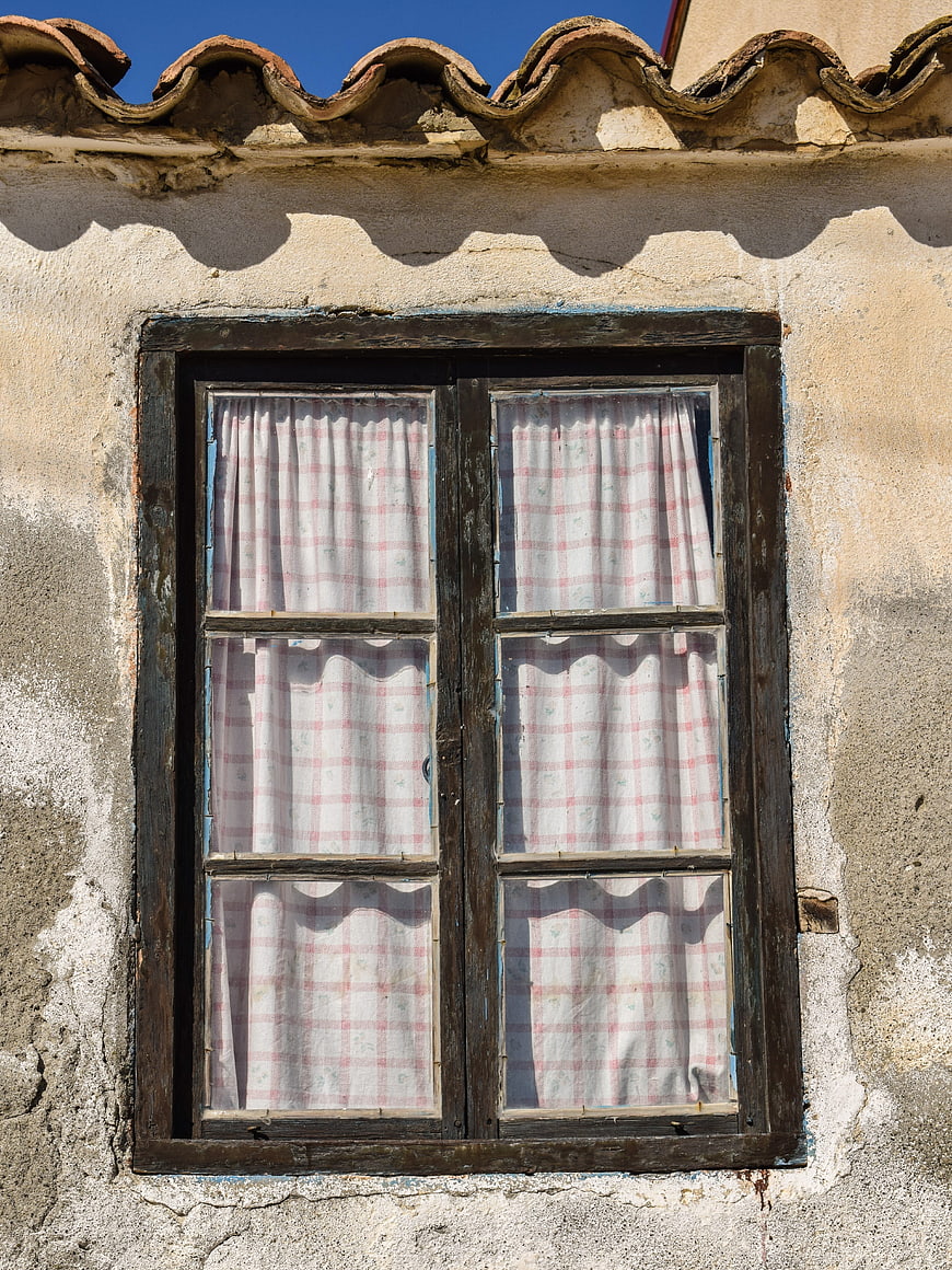 Traditional rustic window with checkered curtains on weathered wall