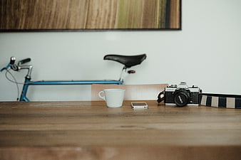 Vintage camera, coffee cup, and smartphone on wooden table with bicycle background