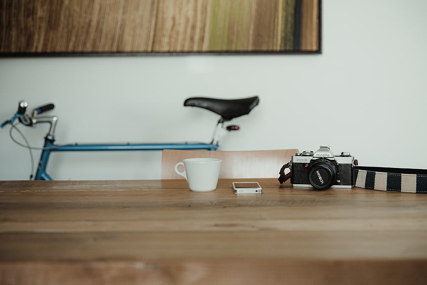 Vintage camera, coffee cup, and smartphone on wooden table with bicycle background