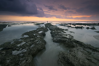 Lone Figure on Rocky Shore at Sunset with Long Exposure