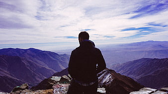 Man standing on mountain peak looking at vast valley landscape