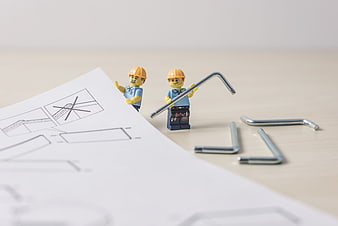 Lego construction workers with blueprints and metal tools on a table