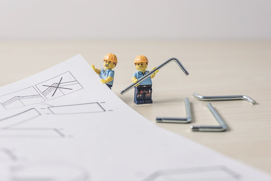 Lego construction workers with blueprints and metal tools on a table