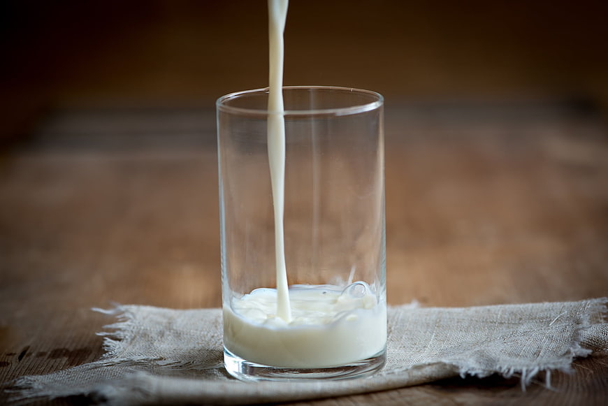 Fresh Milk Pouring into Glass on Wooden Table