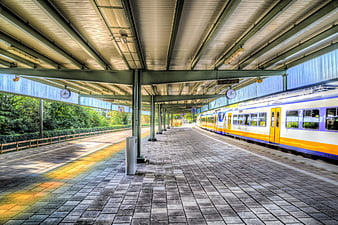 Empty train station platform with yellow and blue commuter train
