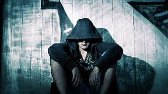 Mysterious hooded figure sitting against textured wall