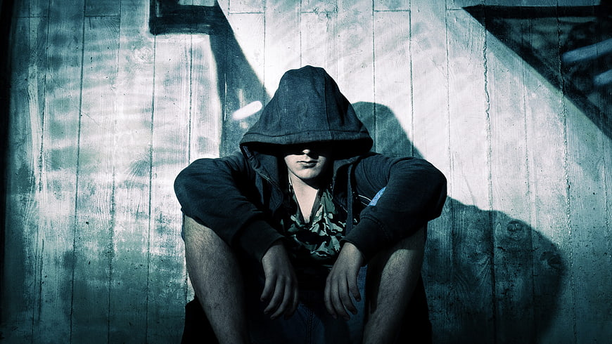 Mysterious hooded figure sitting against textured wall
