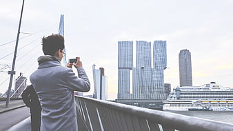Man photographing Rotterdam skyline and cruise ship from bridge