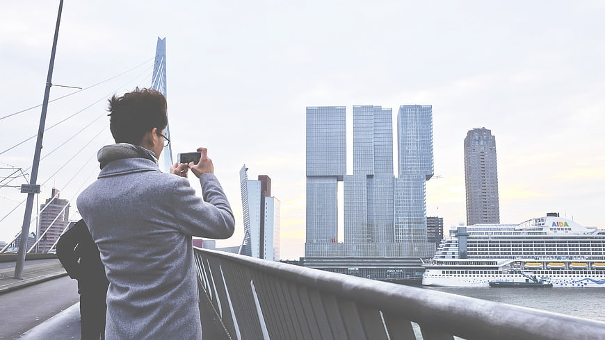 Man photographing Rotterdam skyline and cruise ship from bridge