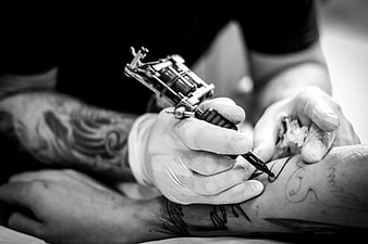Black and white close-up of tattoo artist working on client arm