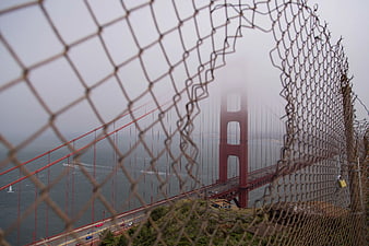 Golden Gate Bridge through chain link fence in fog