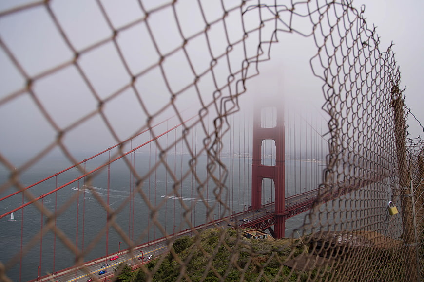 Golden Gate Bridge through chain link fence in fog