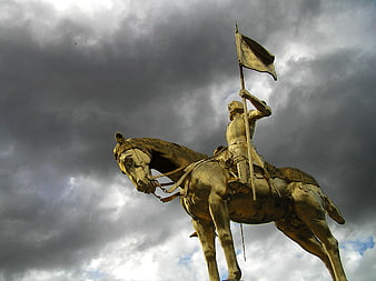 Golden Joan of Arc Equestrian Statue Against Dramatic Dark Cloudy Sky