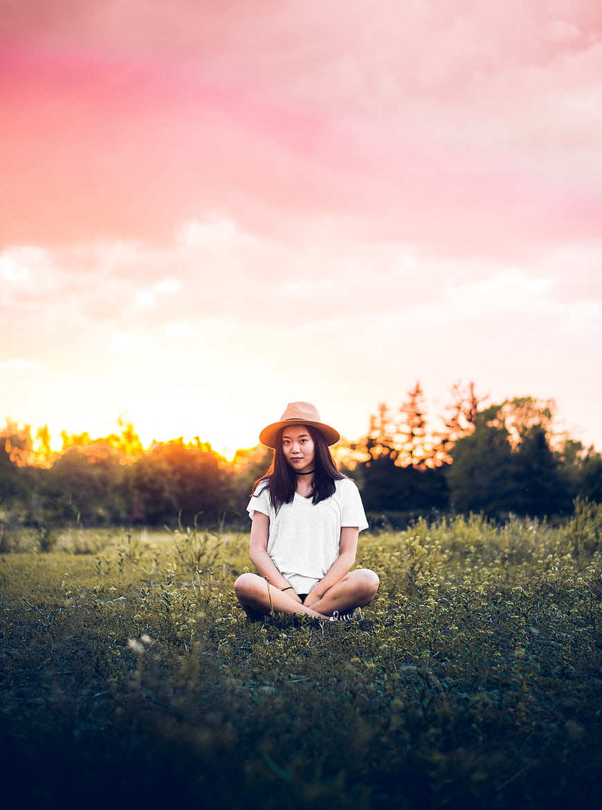 Young woman sitting in grassy field at sunset