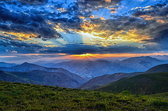 Dramatic Sunset Over Layered Mountain Ranges with Sunbeams