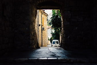 Dark stone archway framing sunlit alley with white van